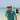 Man in a patterned shirt and hat holding a drink on a boat with clear water and blue sky in the background