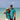 Two people in matching tropical-themed shirts standing on a beach with clear blue water and sky.