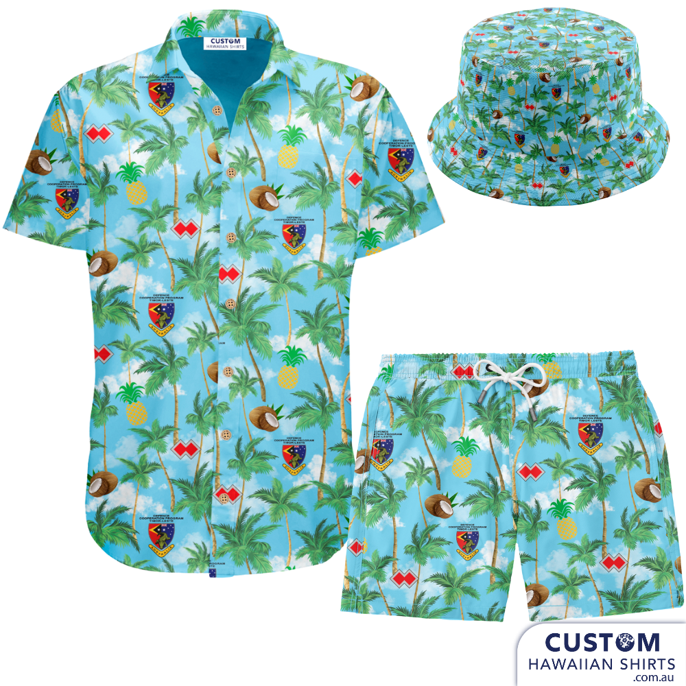 Defence Cooperation Program – Timor Leste  Showcasing some new custom shirts, shorts and bucket hats designed and despatched to Timor Leste to the ADF stationed there. The design features Palms, Pineapples, Coconuts and their logos on a sky blue background with clouds.  Mens Shirts Mens Shorts Bucket hats Embossed coconut buttons