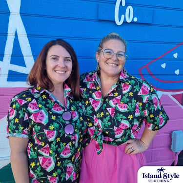 Two women wearing matching outfits with watermelon pattern in front of a colorful mural.