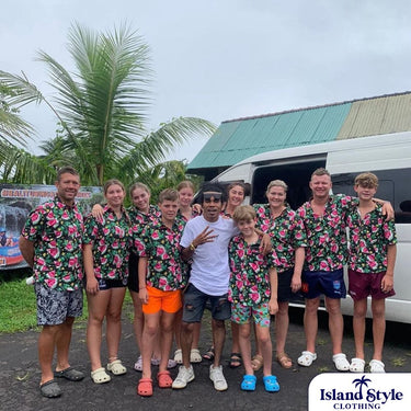Group of people wearing matching floral shirts in front of a white van with palm trees in the background.